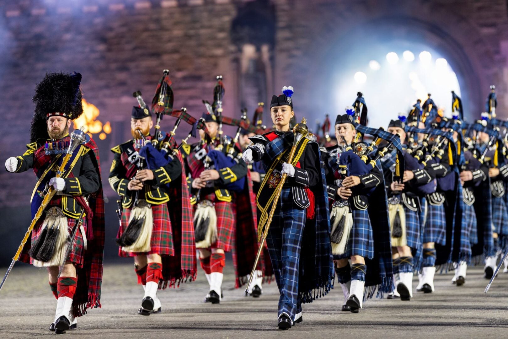 Pipers in traditional Scottish dress of kilts marching through an archway.