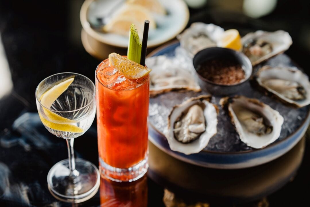 A table laid with a bowl of open oysters and 2 cocktails.