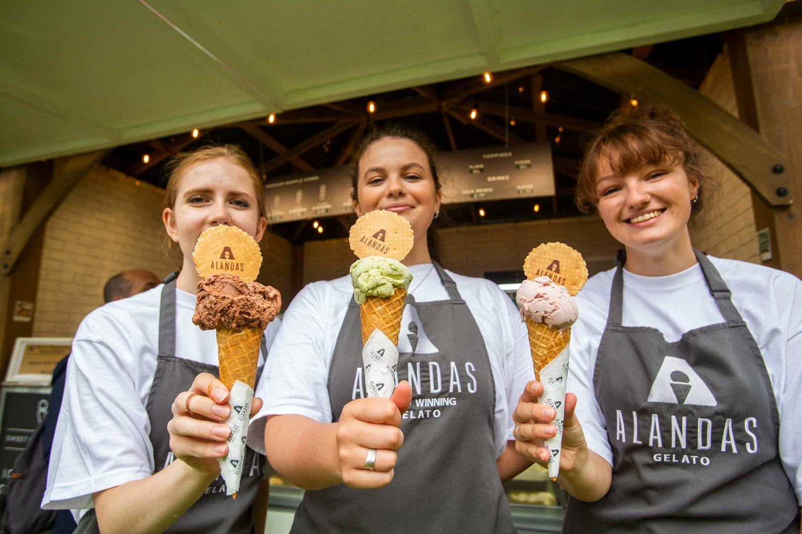 3 people wearing grey aprons, each holding an ice cream cone with a wafer in the top.,© Chris Watt