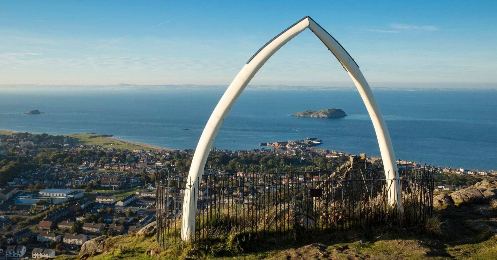 A replica life-size whale's jawbone on the top of a grassy hill, overlooking a coastal town. ,© VisitScotland, Kenny Lam