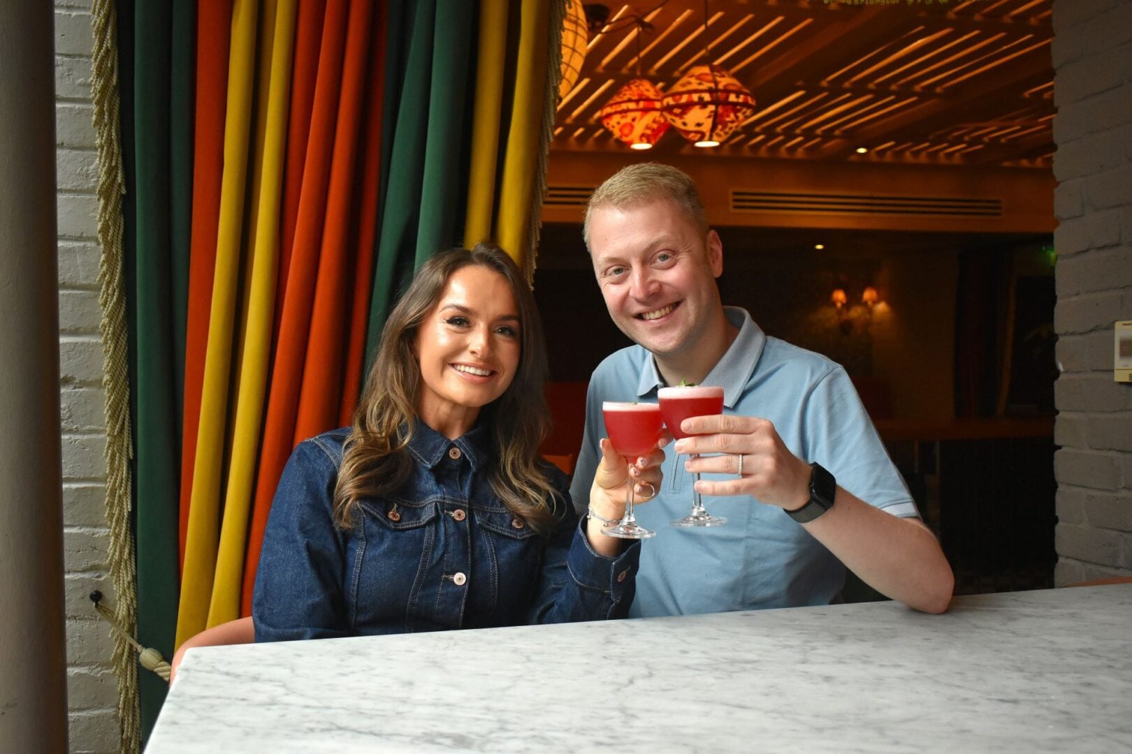 A man and woman sat at a table, each holding a cocktail.