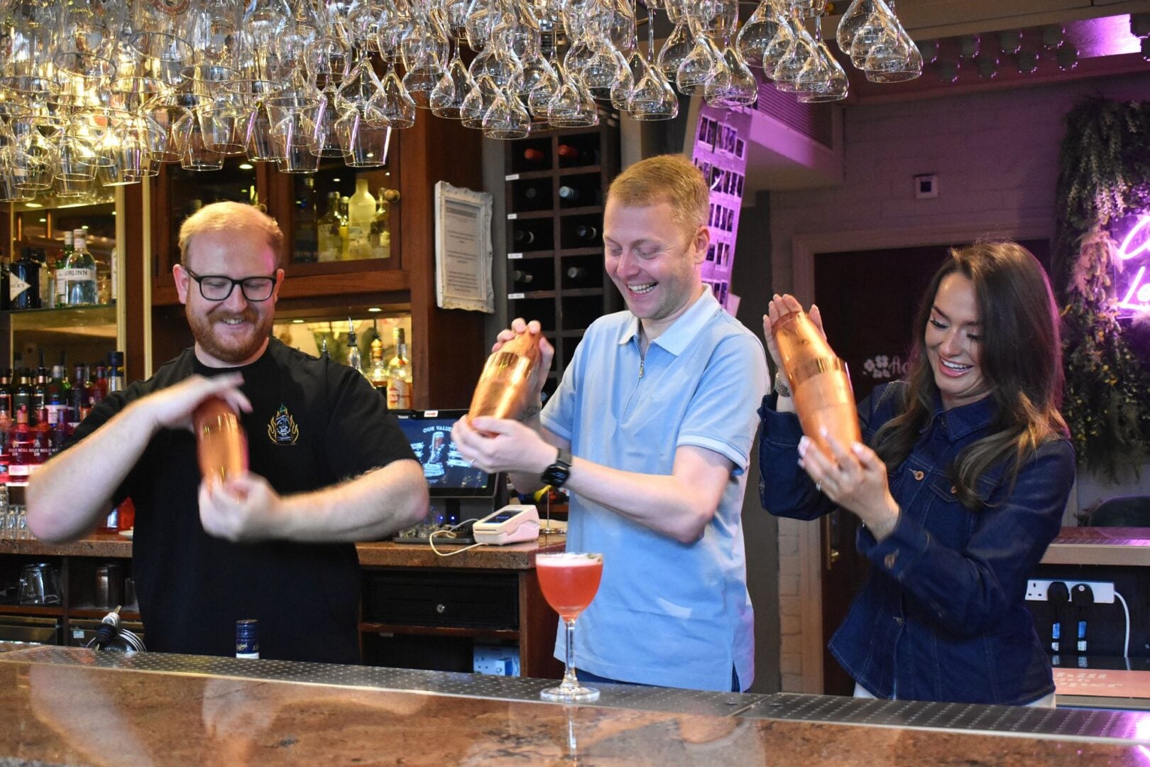 3 people standing behind a bar making cocktails.