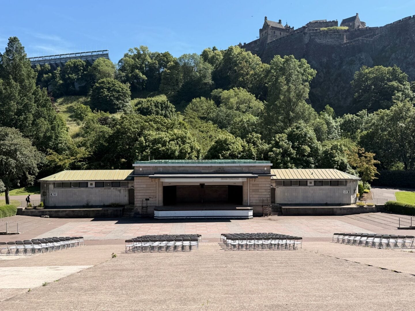 An outdoor stage, set against the backdrop of a rocky hill with a castle on the top.