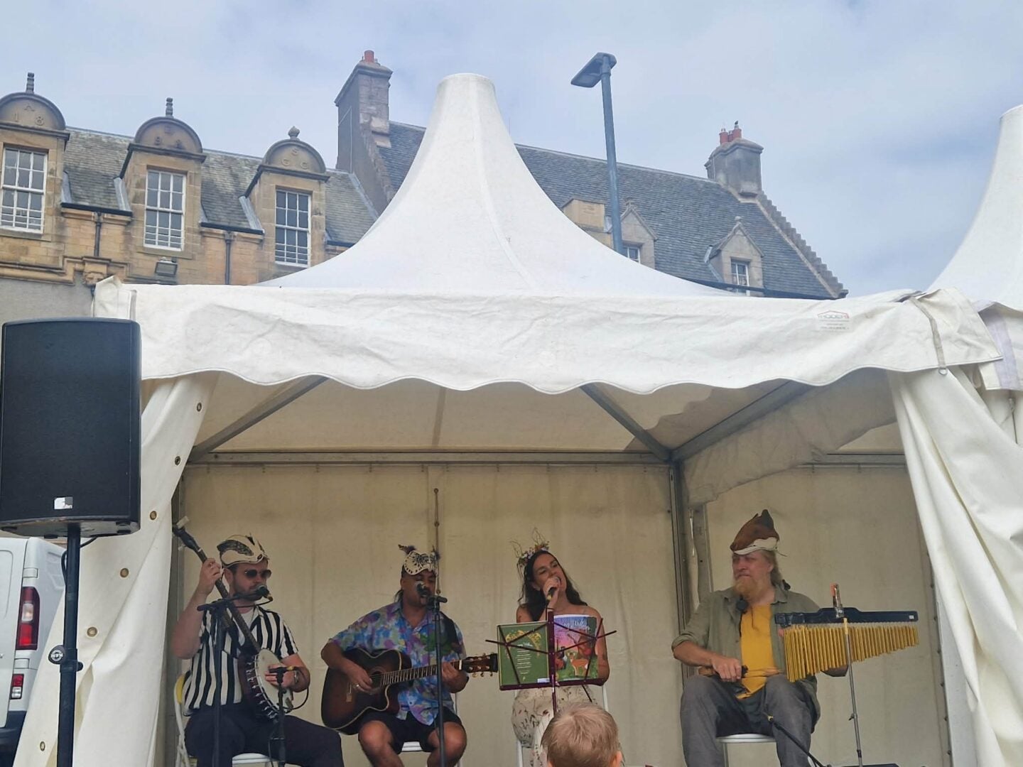 4 musicians in a white tent performing outdoors, against an old stone building.