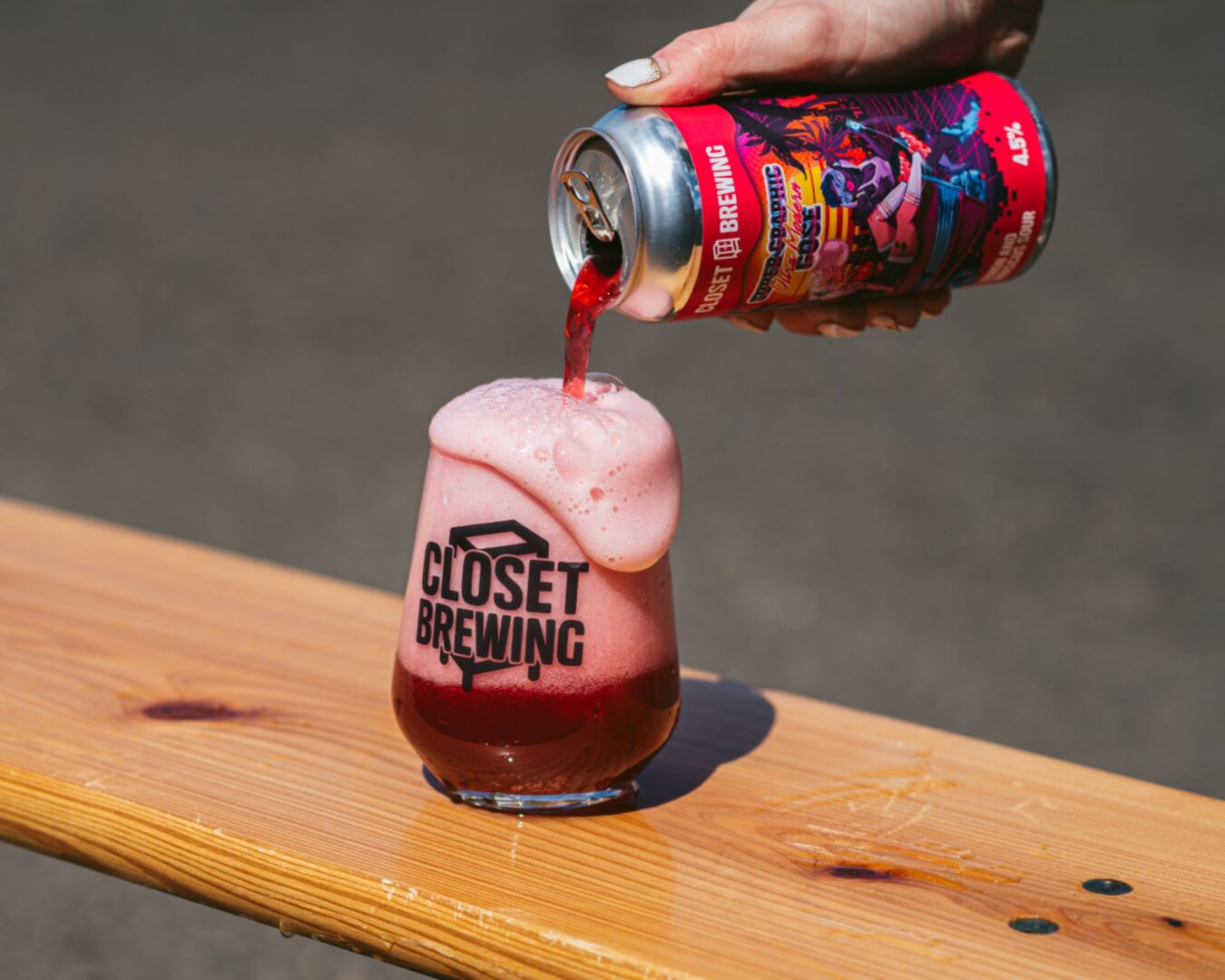 A hand pouring a glass of dark red coloured beer into a glass.