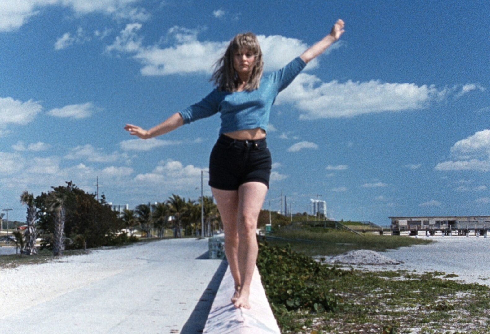 A woman walking along the edge of a prom, with a rocky beach below.