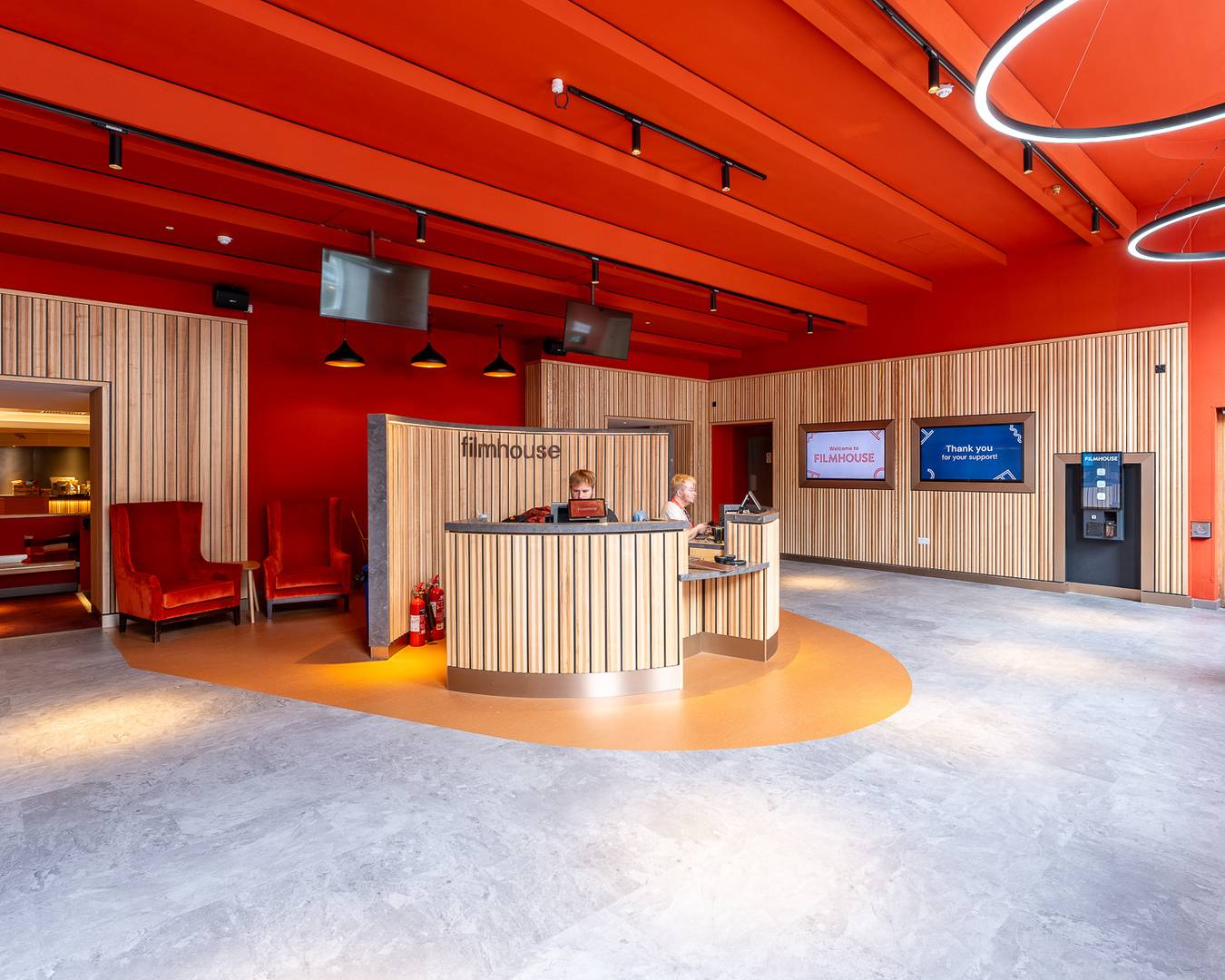 Filmhouse box office, with a circular desk in the centre with wood panelling and wood panelling also on the walls. The ceiling is red. There are two red armchairs to the left.,© Alexander Thomas