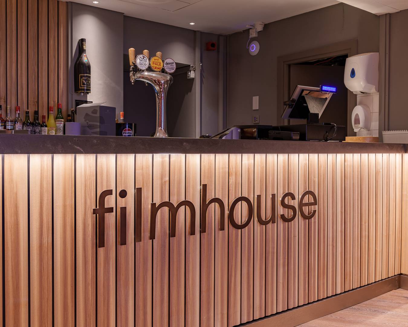 A bar panelled with light ash wood. There is the Filnhouse logo in metal on top of the panels. There is also drinks and beer taps on display.,© Alexander Thomas