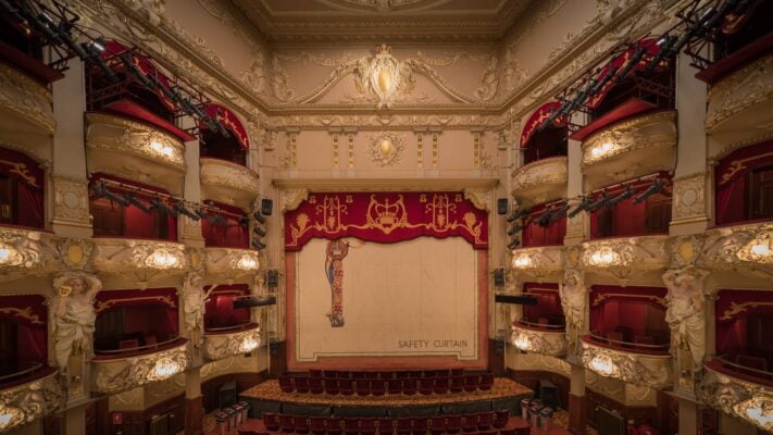 An ornate cream, gold and red theatre with curtains and balconies,© Silke Tuexen