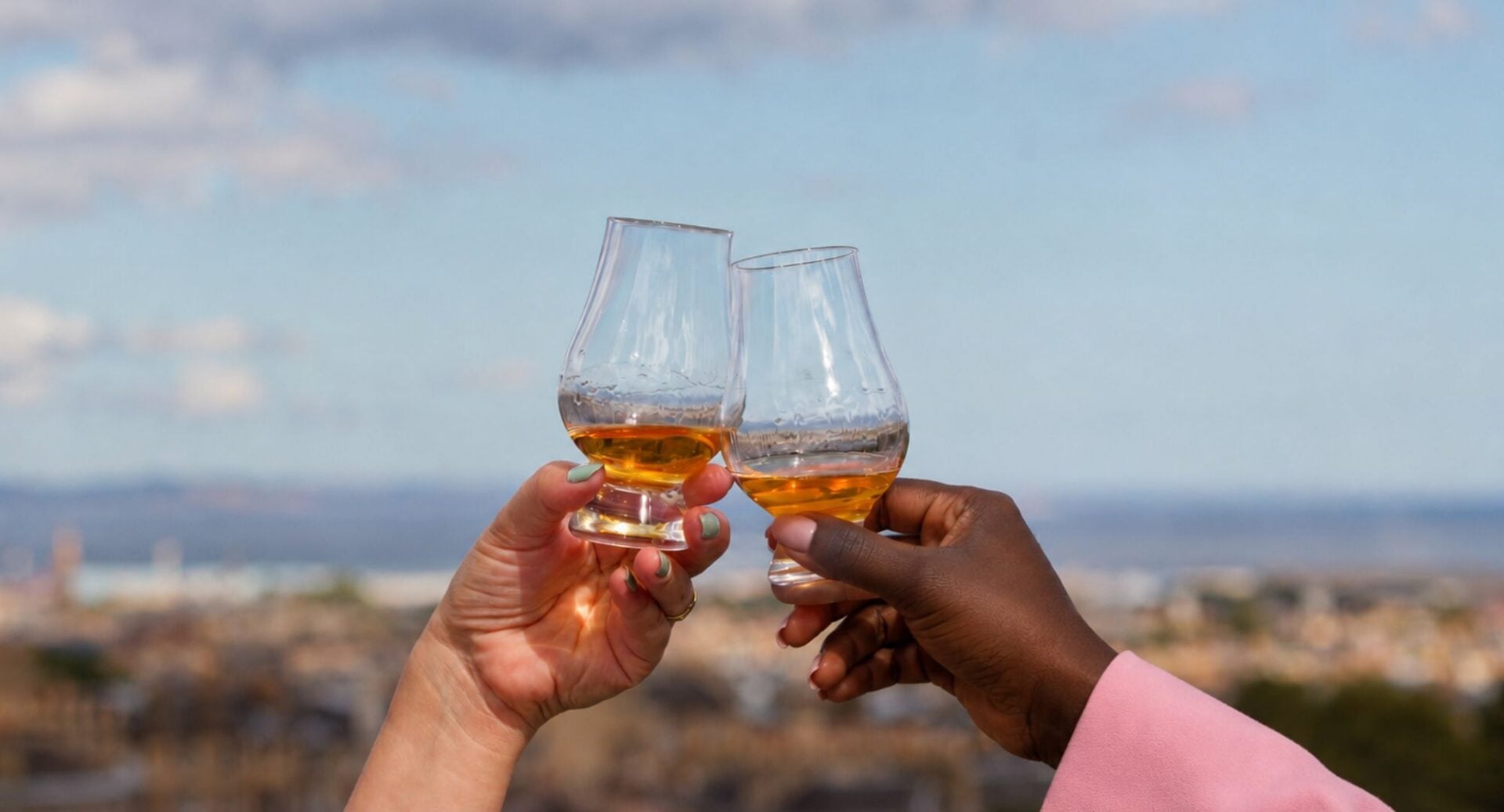 Two glasses being cheered together with a view of Edinburgh skyline behind.