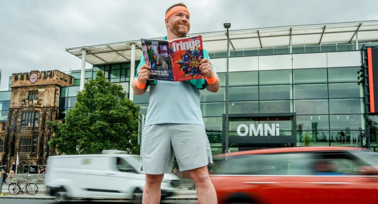 A man holding a brochure, while standing at the side of a road.