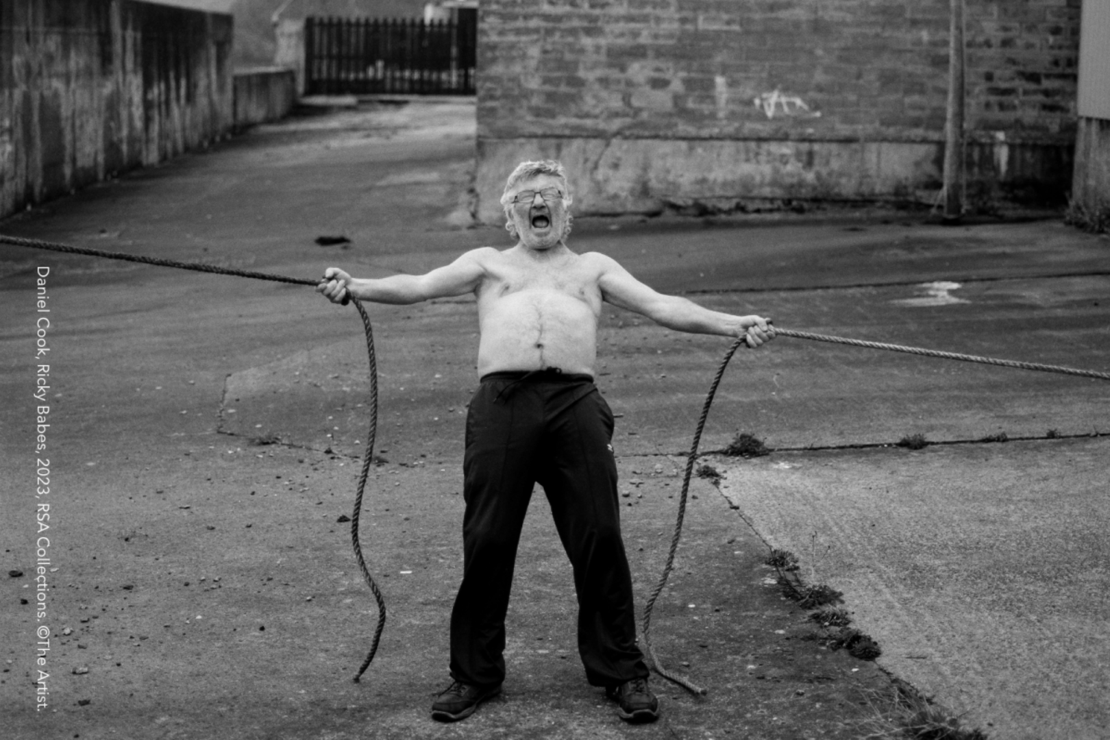 A black and white photo of a man holding 2 bits of rope and shouting.