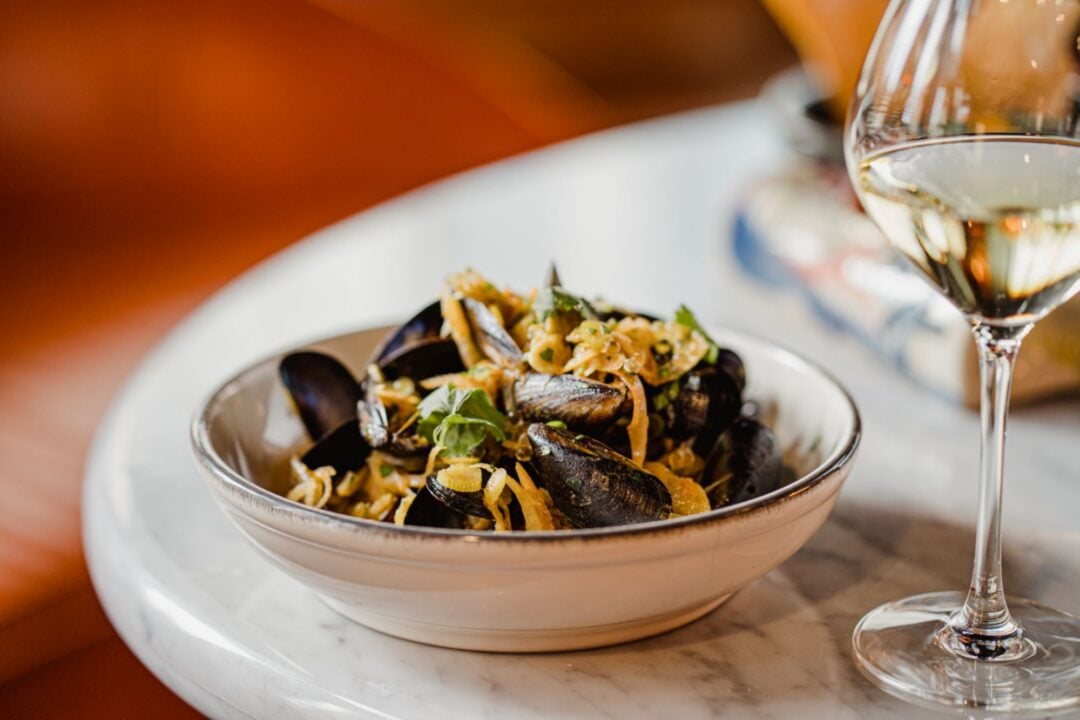 A bowl of mussels, alongside a glass of white wine.