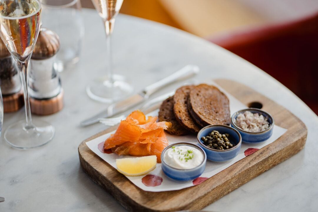 A board set with salmon, brown bread and dips.