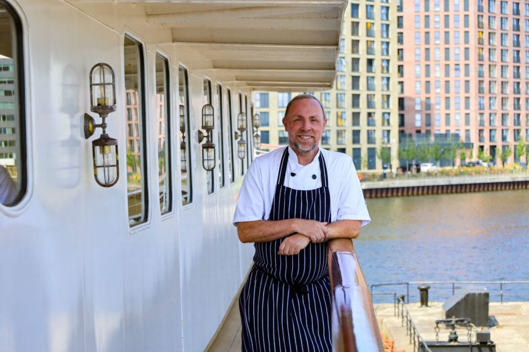 A man in chef's whites standing on the deck of a ship.
