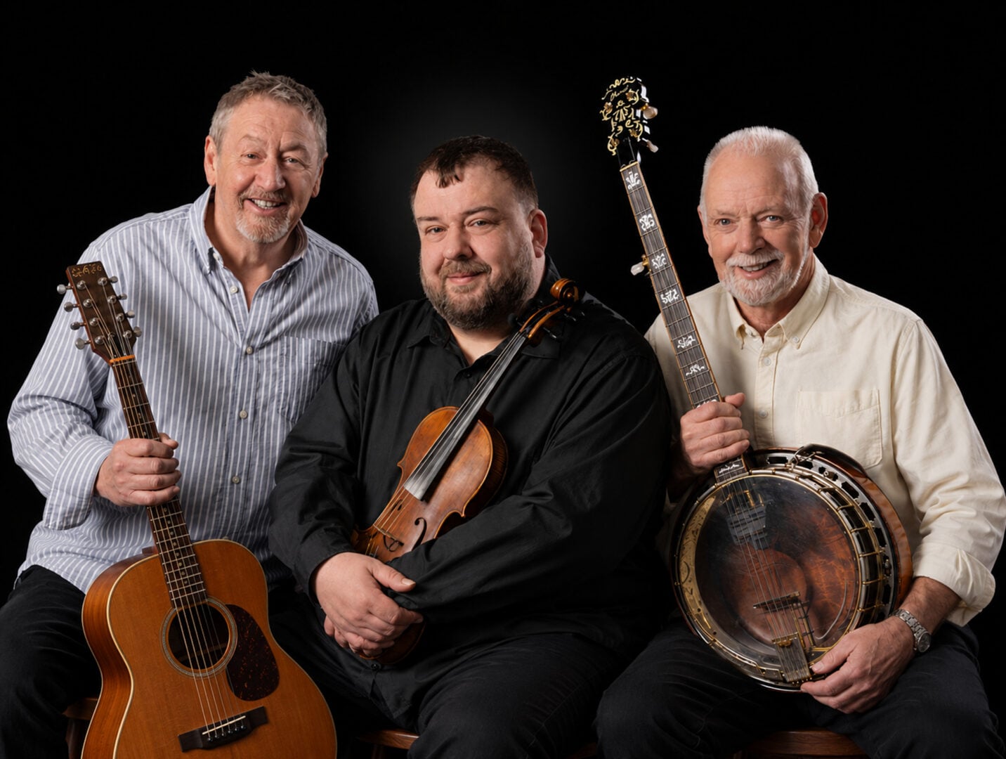 3 seated men, each holding a musical instrument.