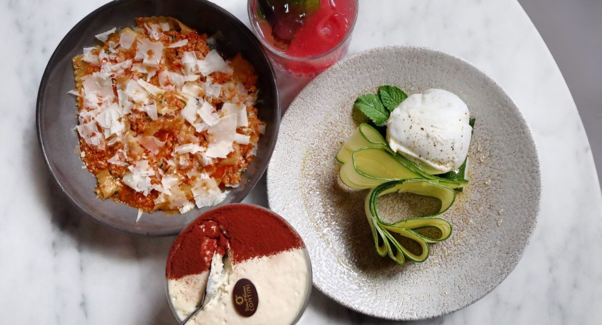A table set with a pasta dish, dessert and cocktail.