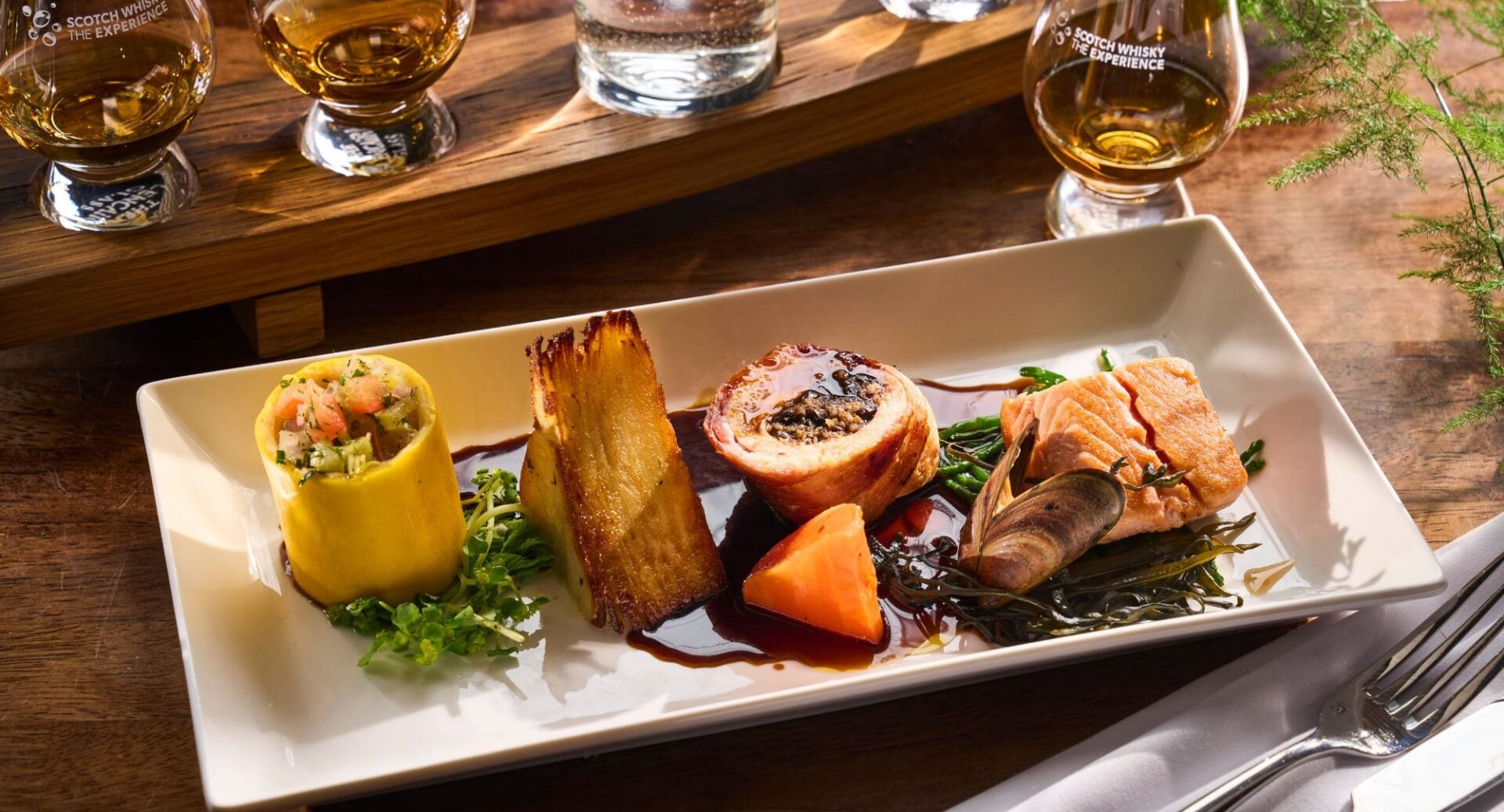 A plate of seasonal meat and fish, beside a flight of whisky glasses.