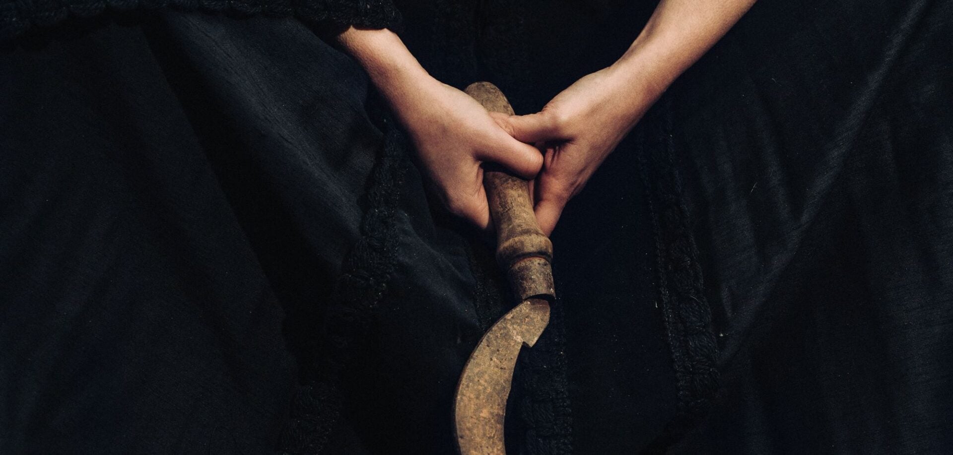 Close-up of a person's hands holding a scythe.