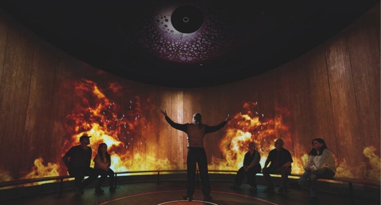 Guide leading tour at Scotch Whisky Experience with screen projection of fire and rain behind where they are sitting