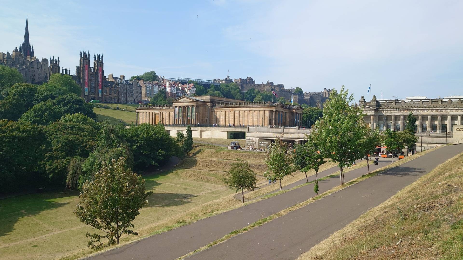 View across central Edinburgh from East Princes Street Gardens, with classical stone buildings, green trees and the Old Town skyline under a blue sky.,© Ross McDowell