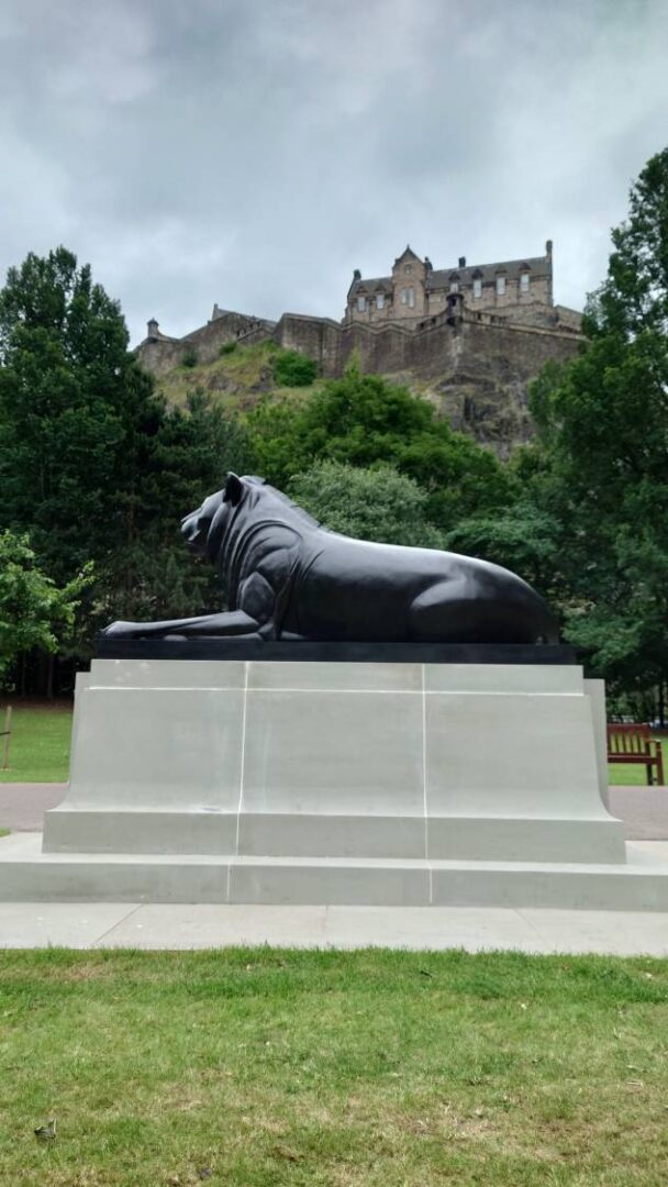 Reclining lion sculpture in Princes Street Gardens, surrounded by trees with Edinburgh’s historic skyline in the background.,© Ross McDowell