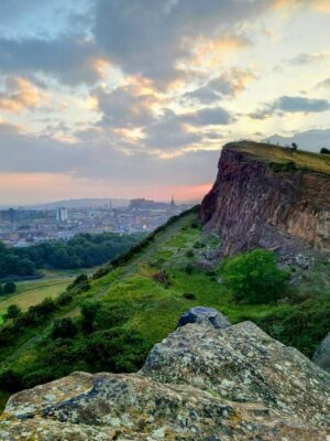 Salisbury Crags in Holyrood Park overlooking Edinburgh, with the city skyline and Edinburgh Castle visible in the distance.,© Ross McDowell