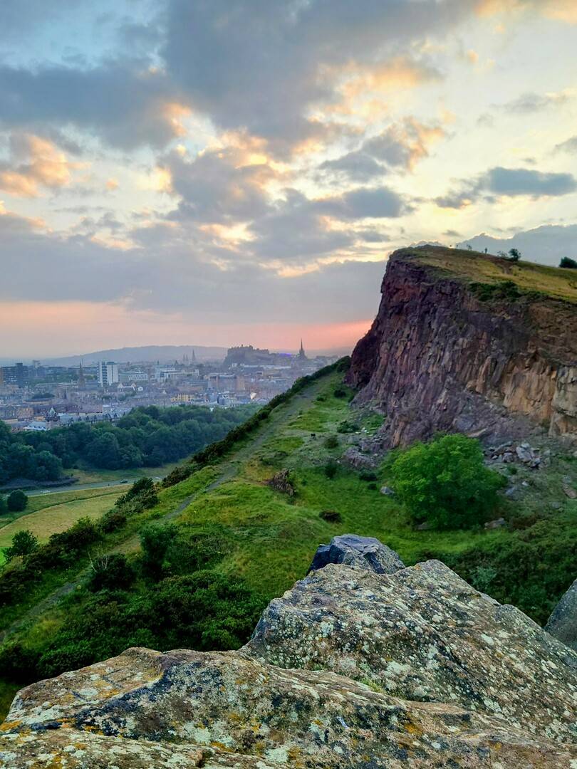 Salisbury Crags in Holyrood Park overlooking Edinburgh, with the city skyline and Edinburgh Castle visible in the distance.,© Ross McDowell
