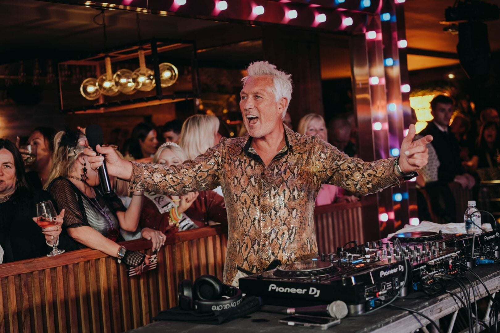 A man at a DJ stand entertaining a crowd of people.