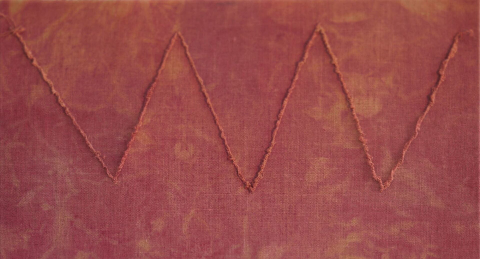 Zip zag line across a dark red piece of fabric.