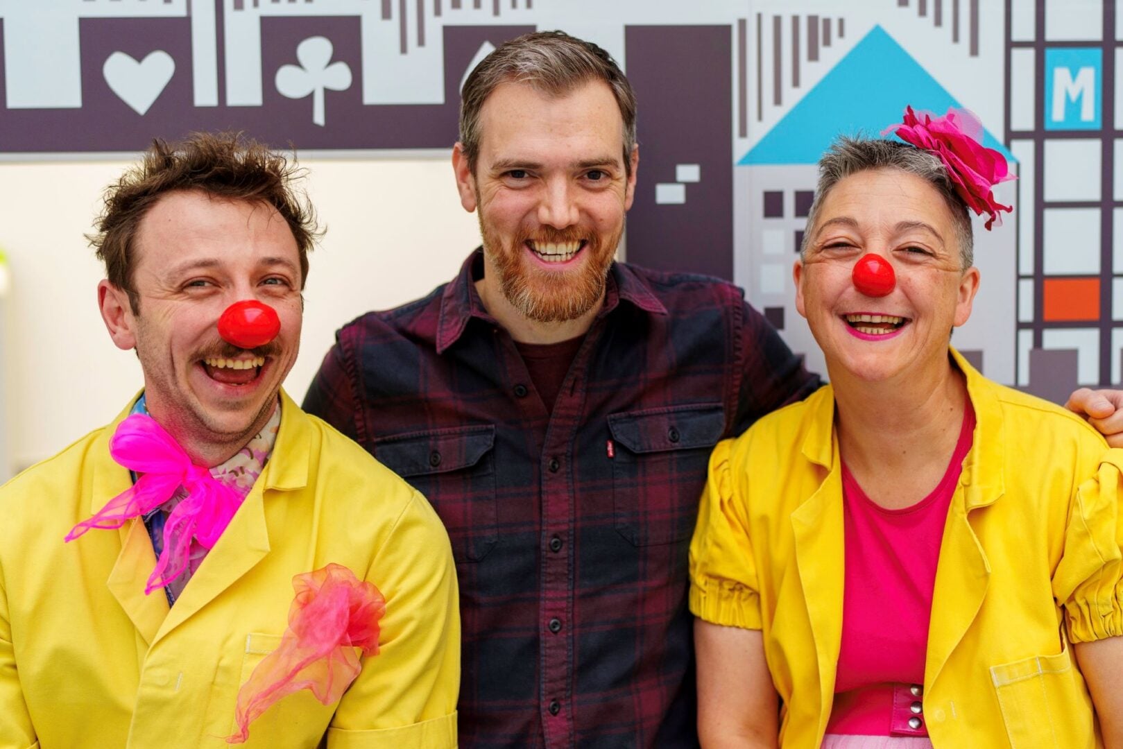 3 people standing in a row, 2 of whom are wearing fake red clown noses.