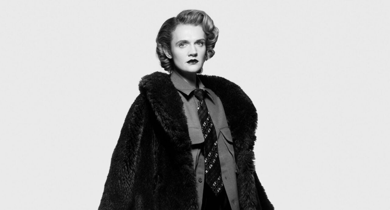 Black and white image of a woman wearing a shirt and tie, and fur coat.
