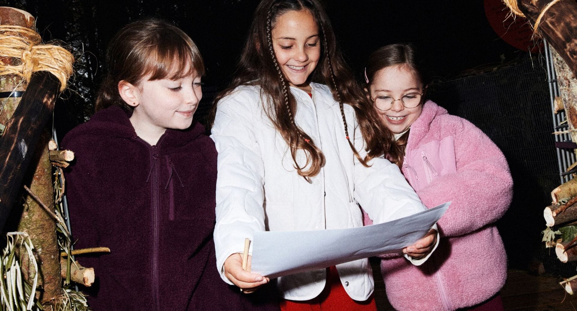 3 young girls looking at a large sheet of paper in front of them.
