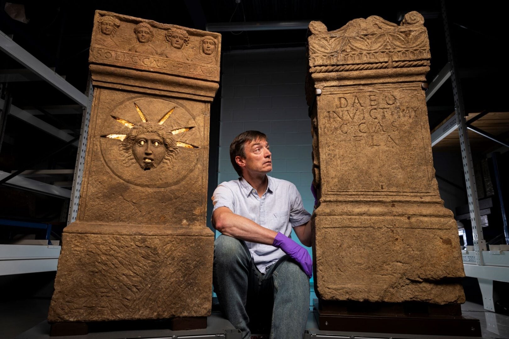 A man crouched down beside 2 stone altars.