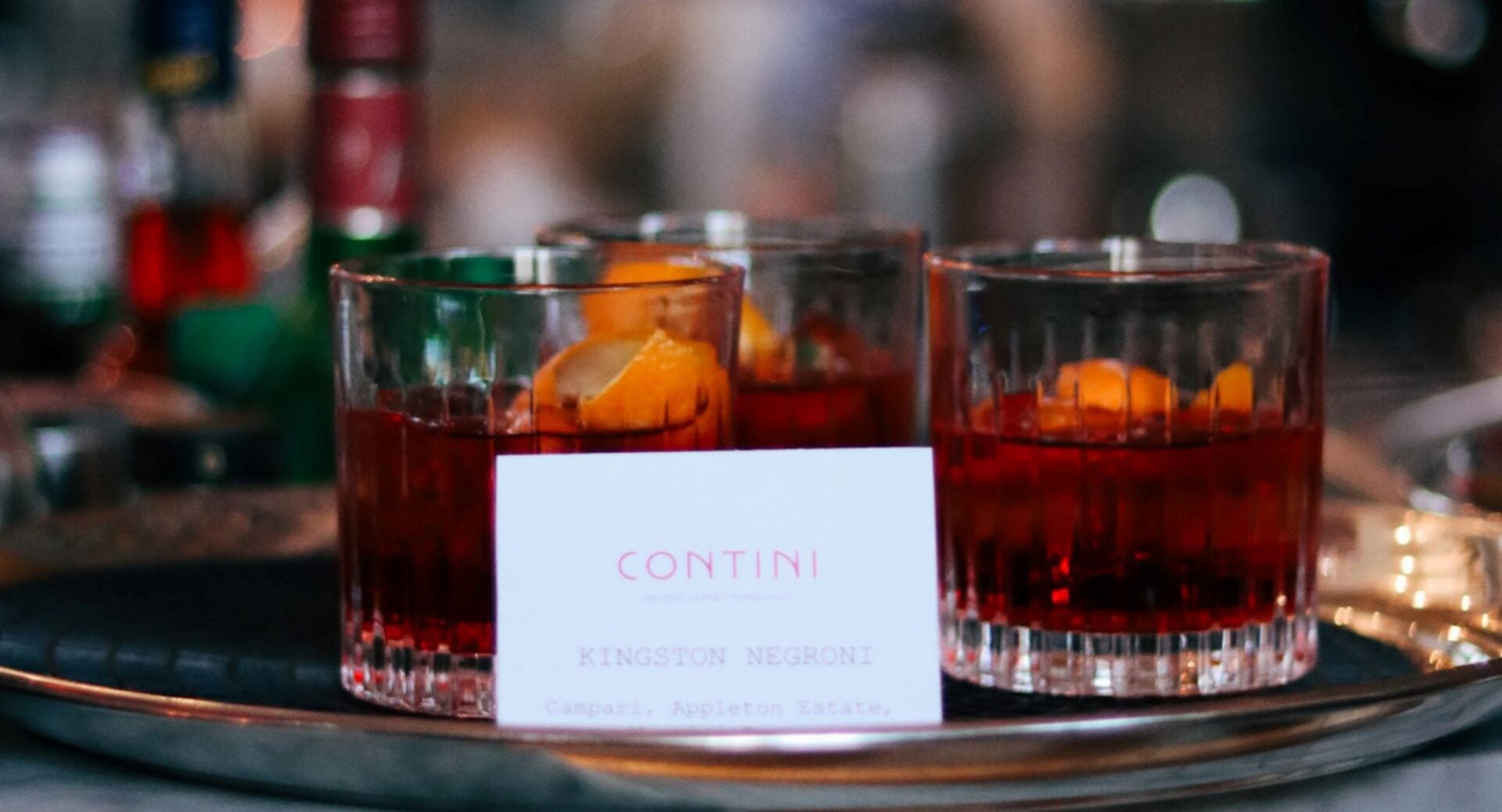 Close-up of 3 glasses, filled with dark red liquid, on a tray.