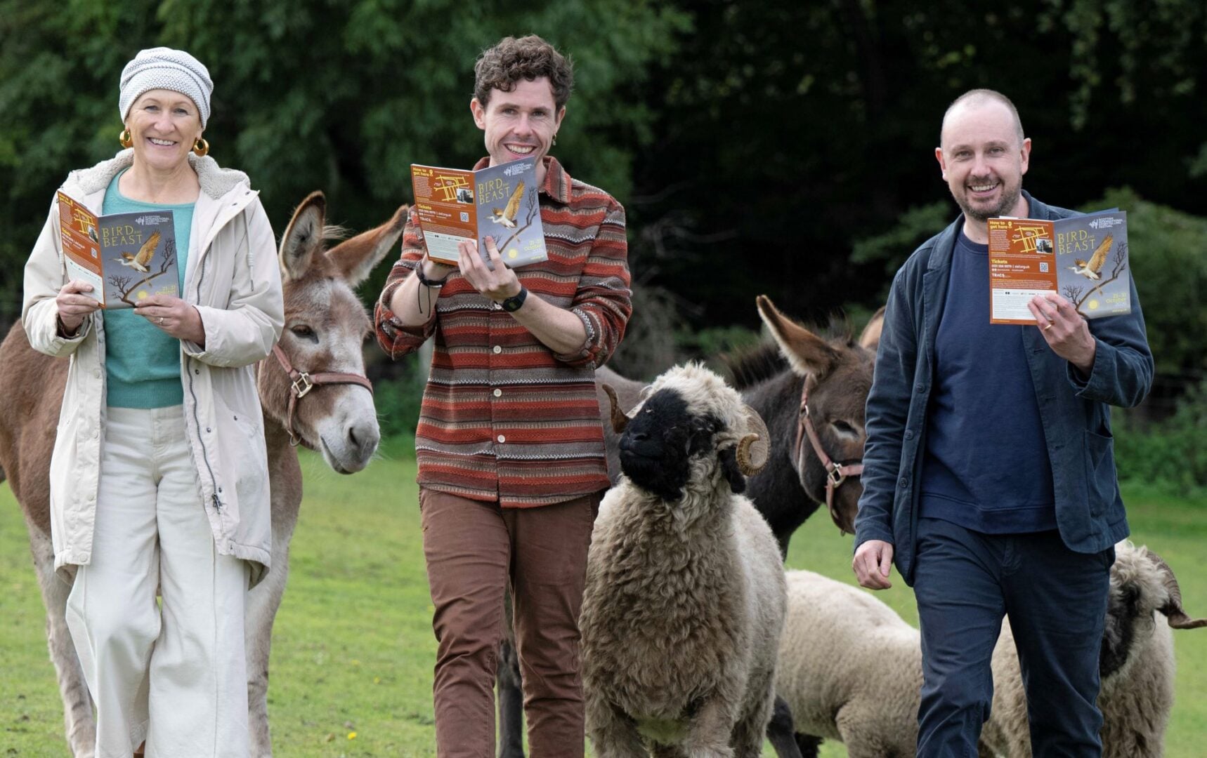 3 people, each holding a small booklet, walking in a line, with donkeys and sheep behind them.
