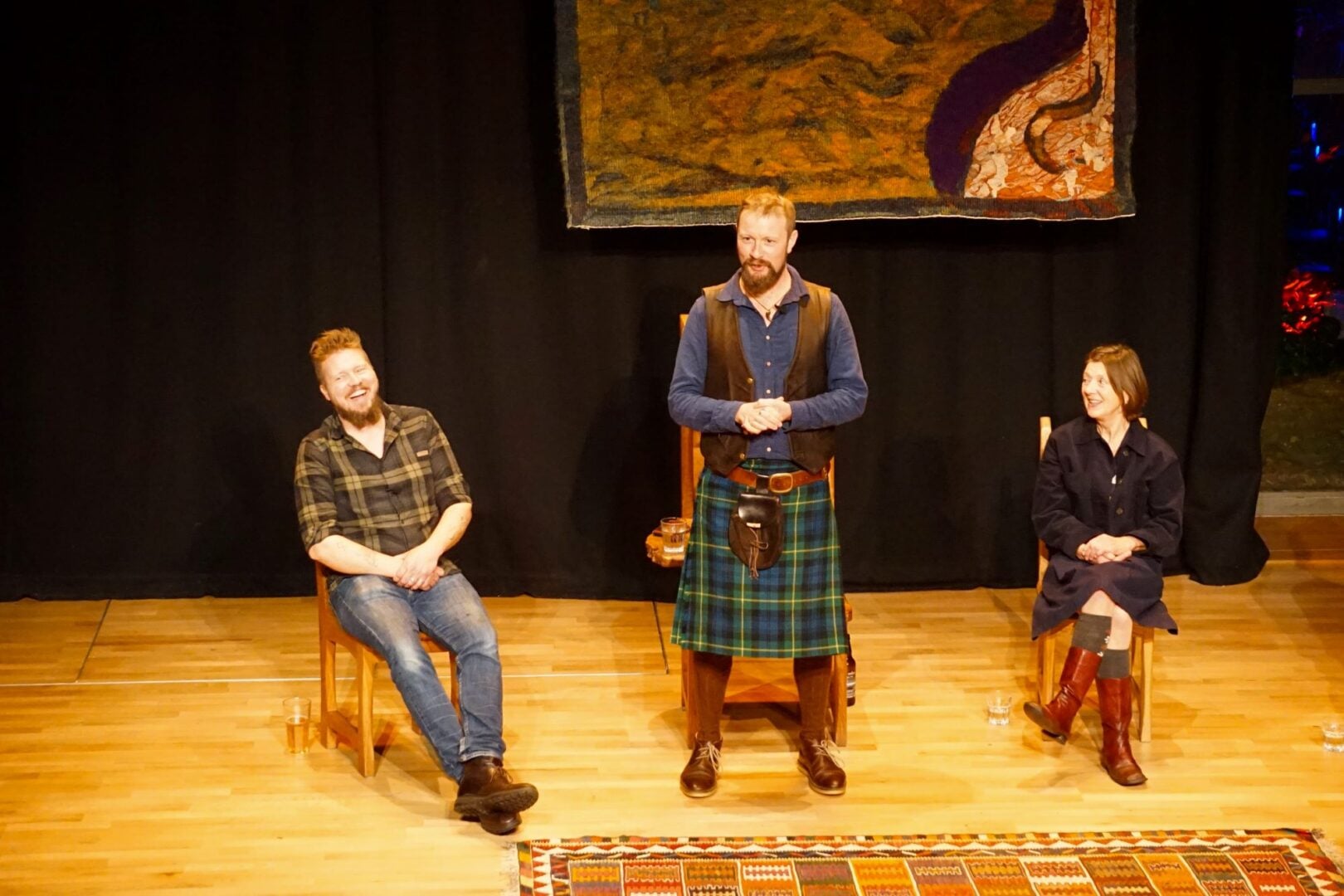 3 people on a stage, the middle person standing.