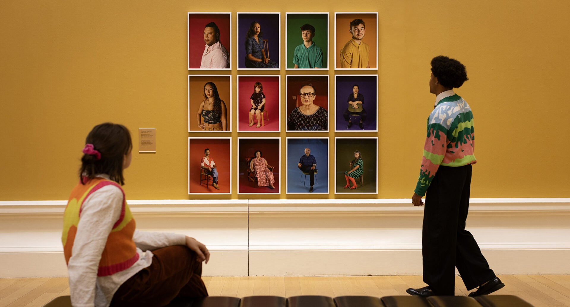 A couple looking at wall, on which there are a collage of portraits.