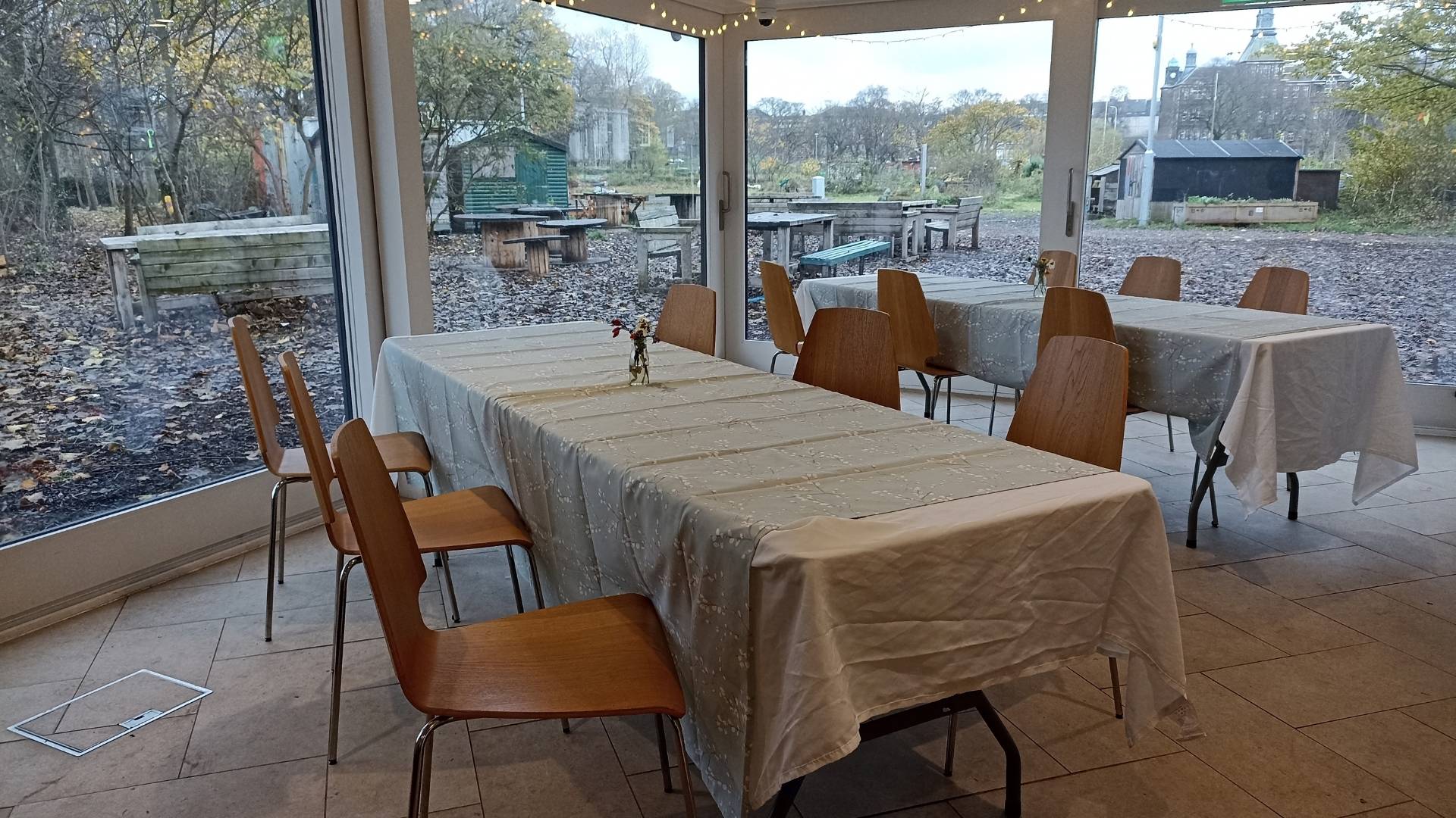 The garden room at Leith Community Croft. A large bright room with large floor to ceiling windows. Two long tables with chairs either side sit in the middle of the rooms,© Earth in Common