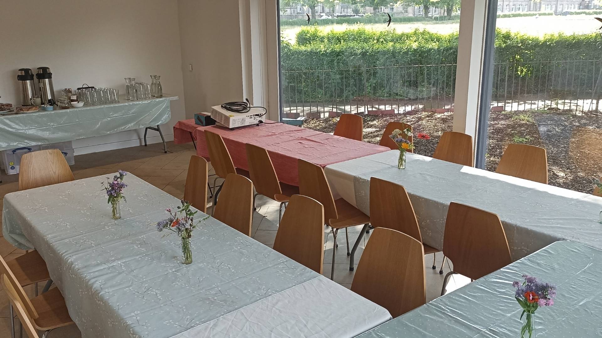 A view of the garden room on Leith Community Croft. A large bright room with floor to ceiling windows. Tables and chair set up in a u shape ready for an event.,© Earth in Common