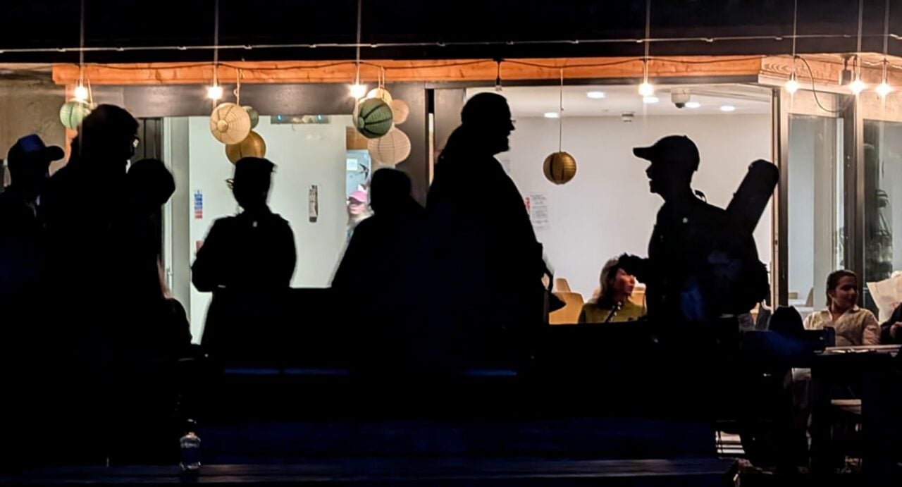 Silhouettes of people standing in a room, with people sitting behind them.