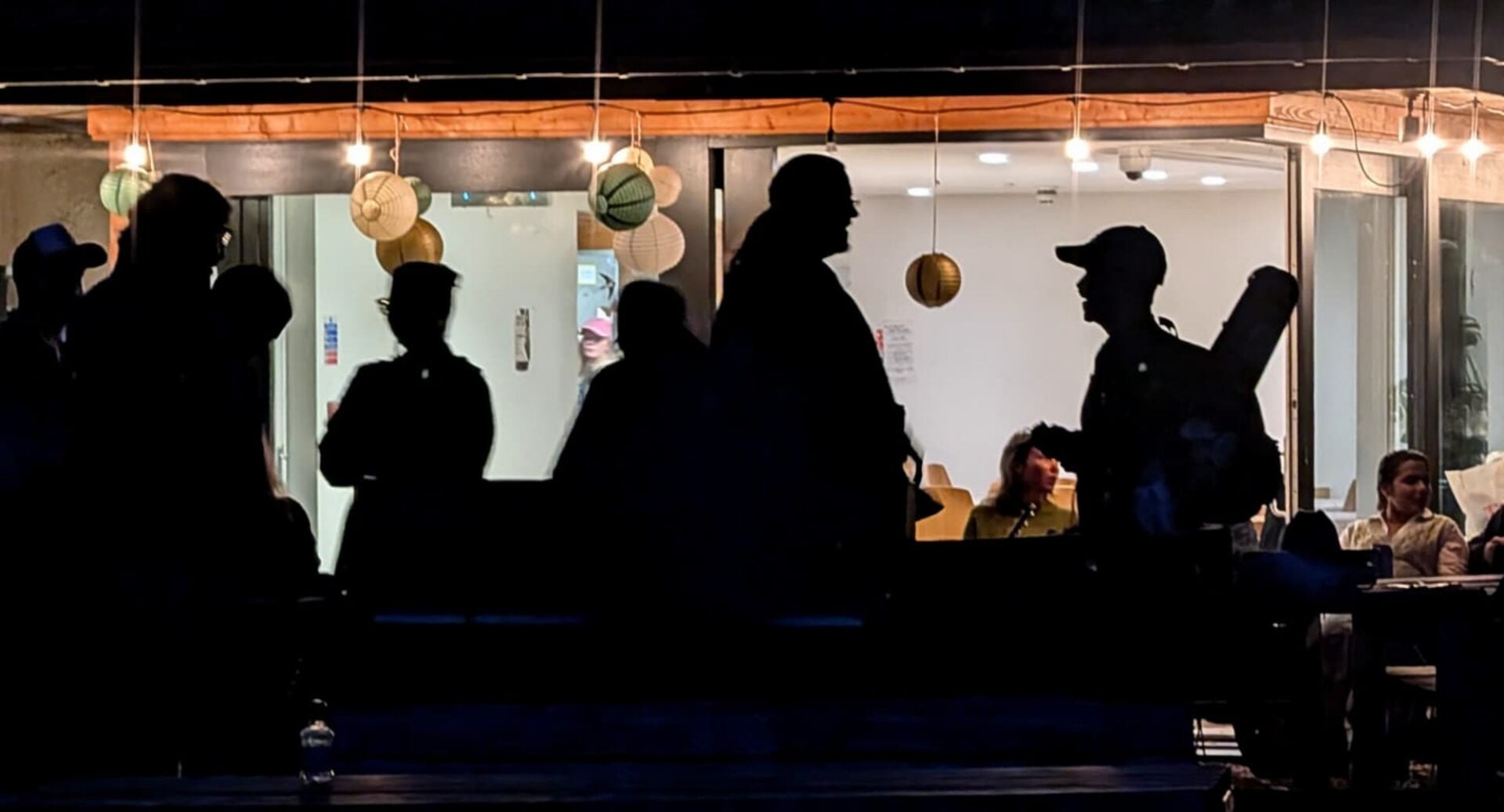 Silhouettes of people standing in a room, with people sitting behind them.