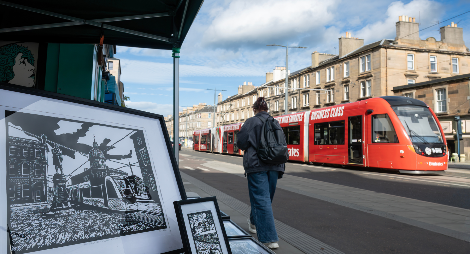 A tram runs along Leith Walk past a shop front selling an illustration of a tram as woman walks past.