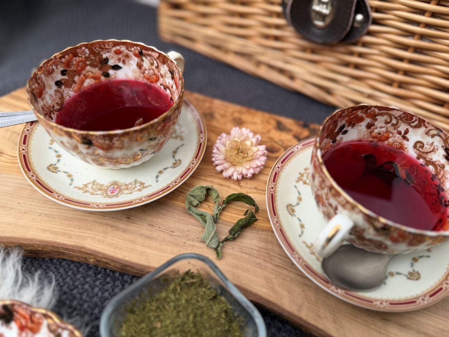 A basket, with 2 china tea cups and flower petals.