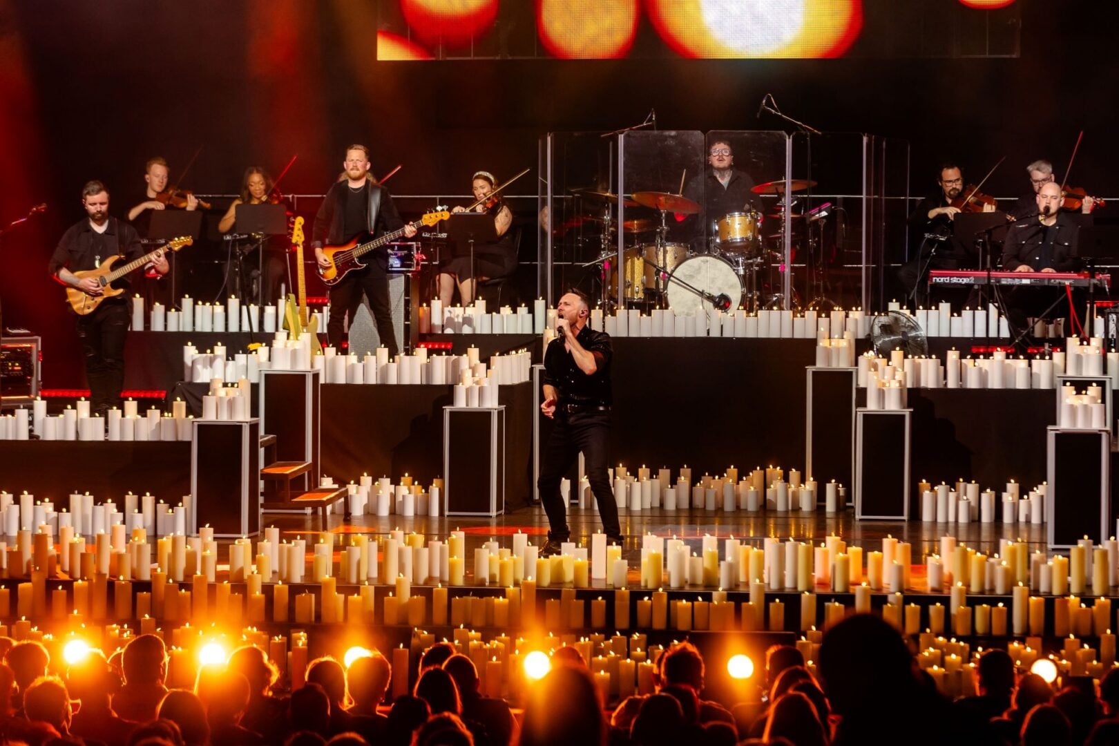 An orchestra and singer performing on stage, in front of several light candles.