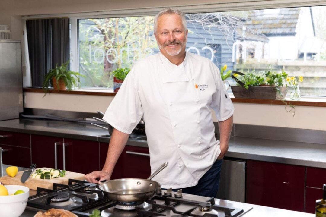 A man wearing chef's whites, standing in a kitchen.