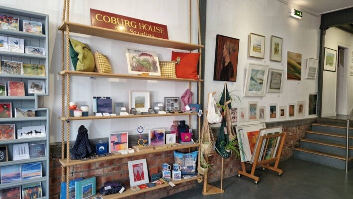 rope shelving displaying handmade paintings, cushions, jewellery, plant hangers. Paintings on the wall.