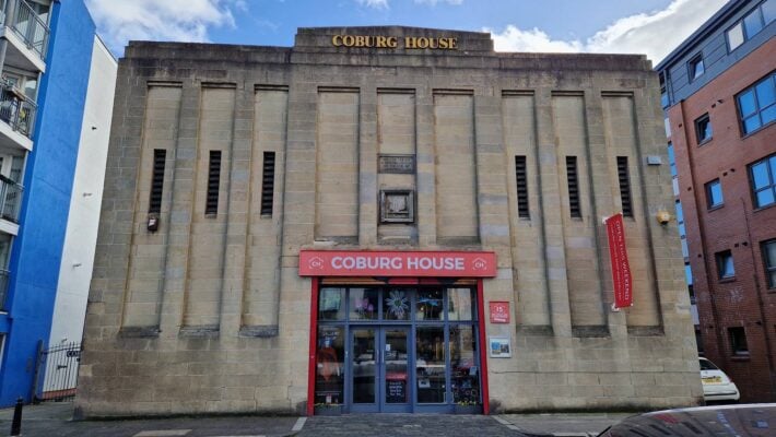 Outside Coburg House. Large brick building with big red Coburg sign and glass door entrance.