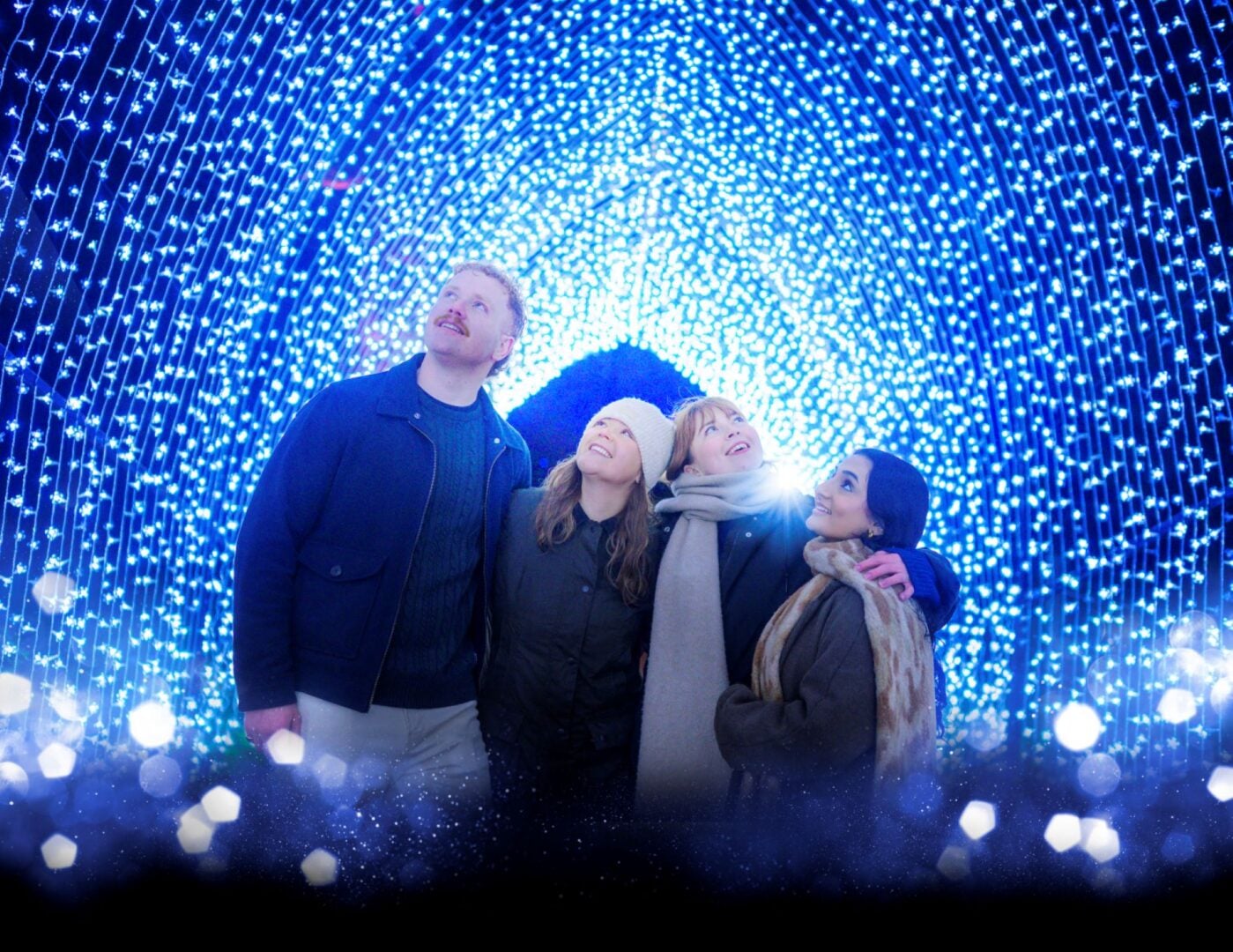 A group of people standing in an illuminated tunnel of lights.
