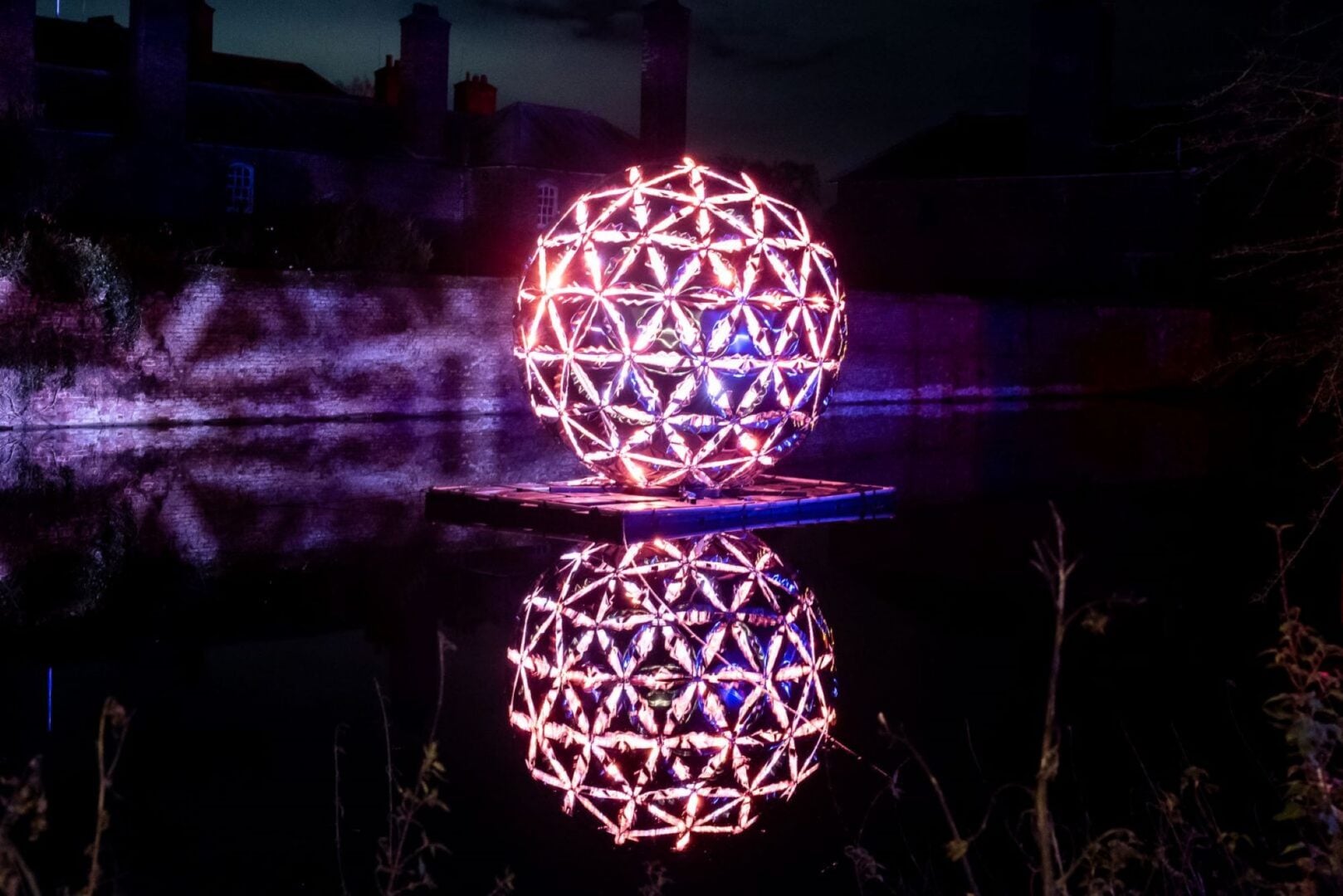 An illuminated sphere sitting on a platform on a body of water.